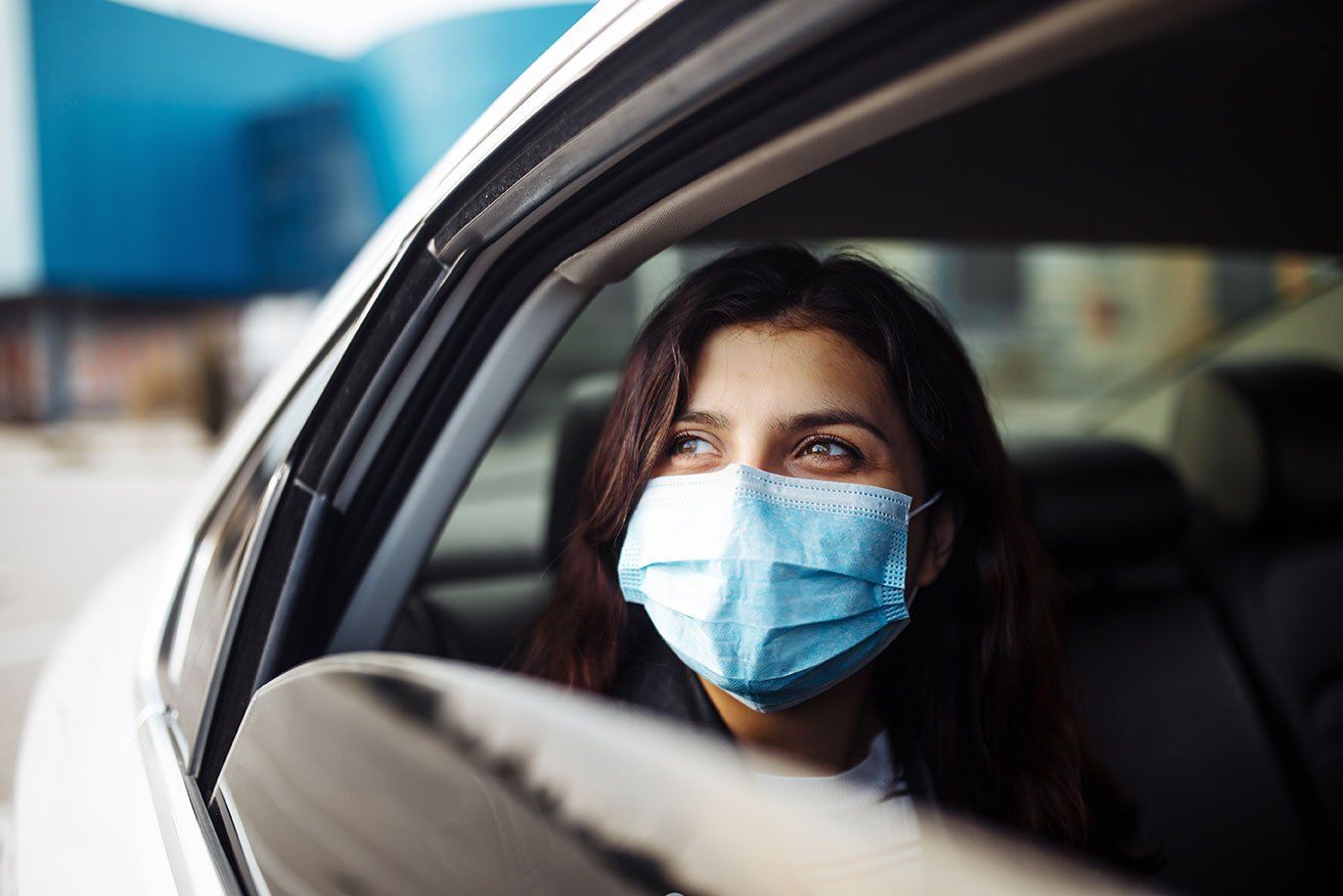 Femme à l'arrière d'un taxi portant un masque