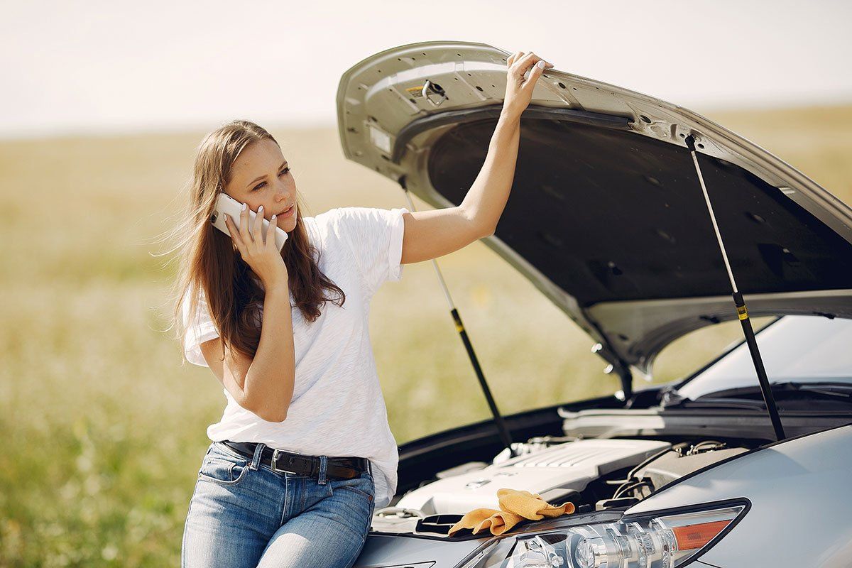 Femme en panne de voiture au bord de la route, en train d'appeler l'assistance