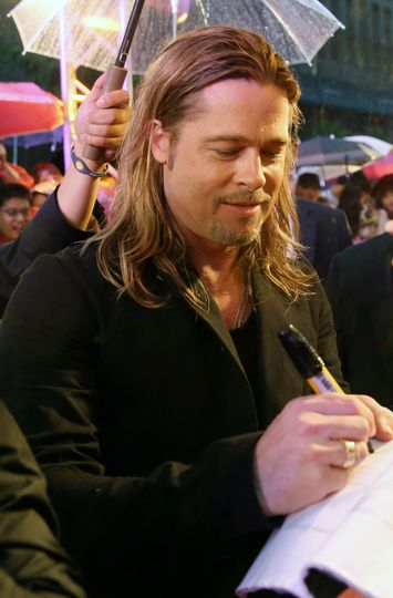 Person with wet hair signing an autograph under a clear umbrella at an event.