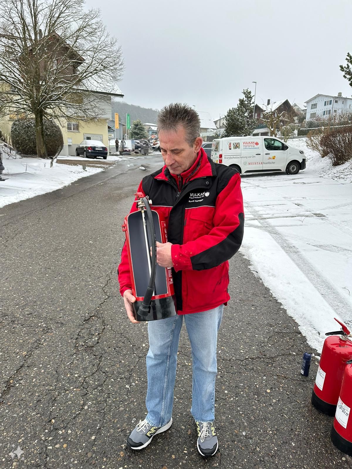 Ein Mann in einer roten Jacke steht auf einer verschneiten Straße und hält eine Trophäe in der Hand.