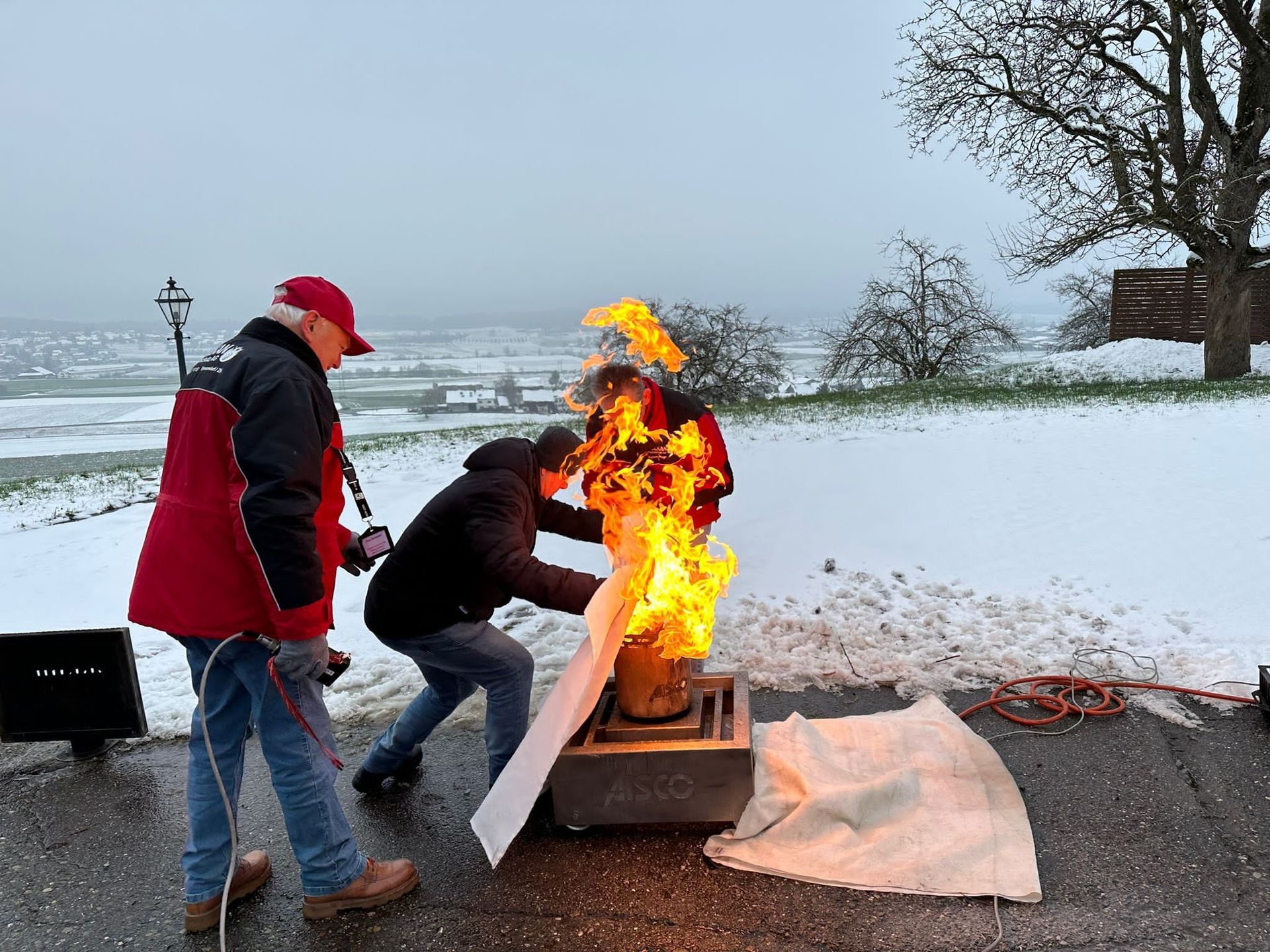 Zwei Männer stehen vor einem Feuer im Schnee.