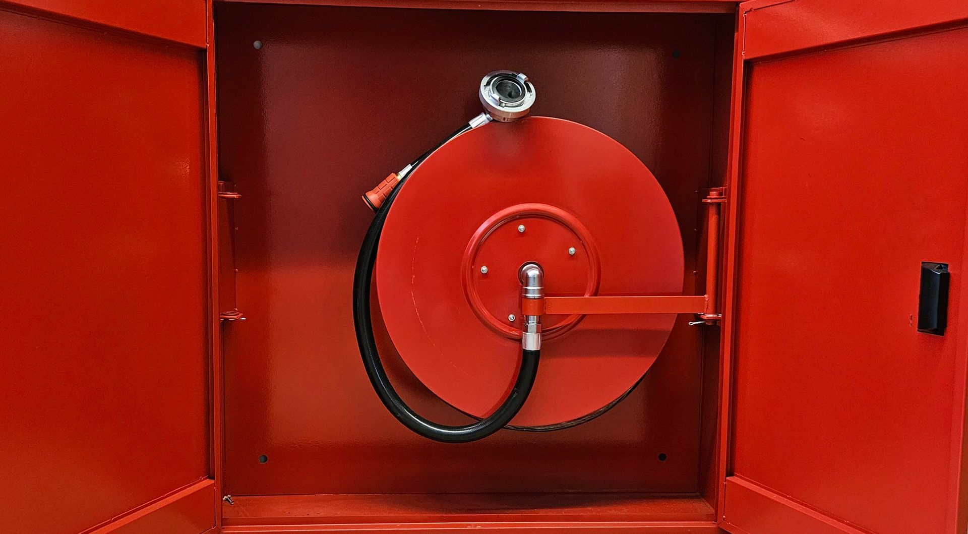 Eine rote Feuerwehrschlauchtrommel, an der ein schwarzer Schlauch befestigt ist.