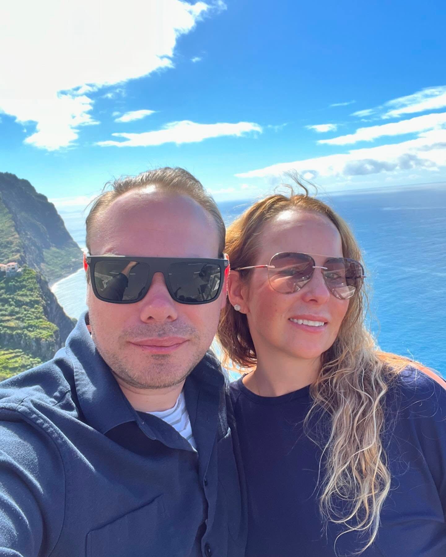 Two people in sunglasses taking a selfie by the ocean under a bright blue sky