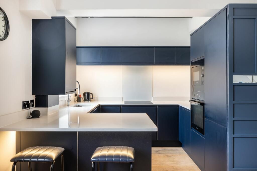 Modern navy-and-white kitchen with island, glossy cabinets, built-in oven, and two black stools