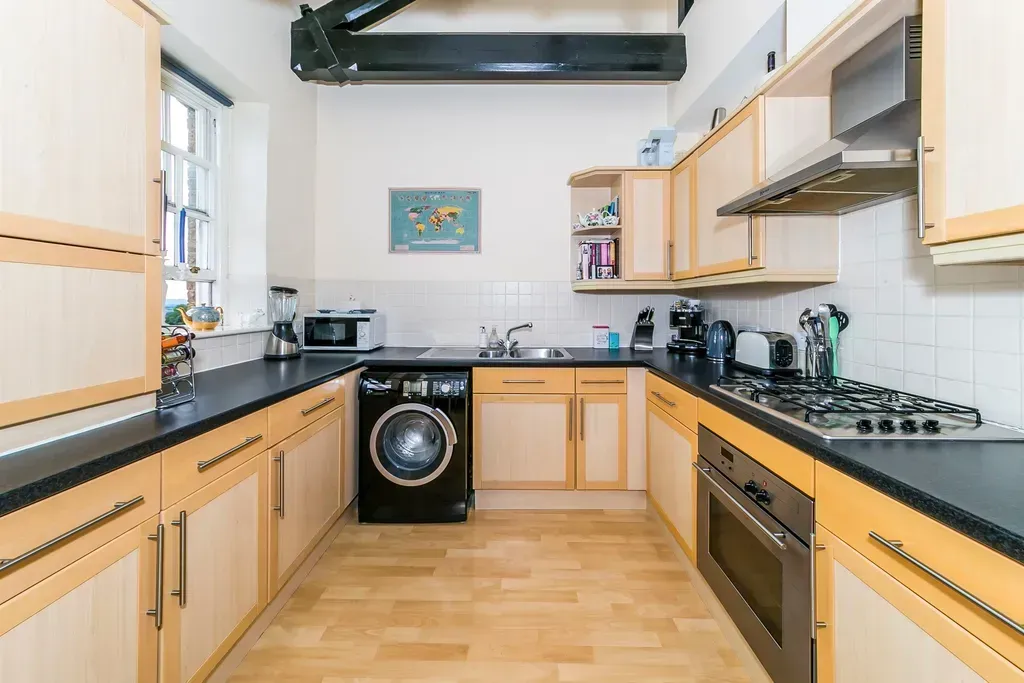 Bright modern kitchen with wooden cabinets, black countertops, and appliances along both sides.