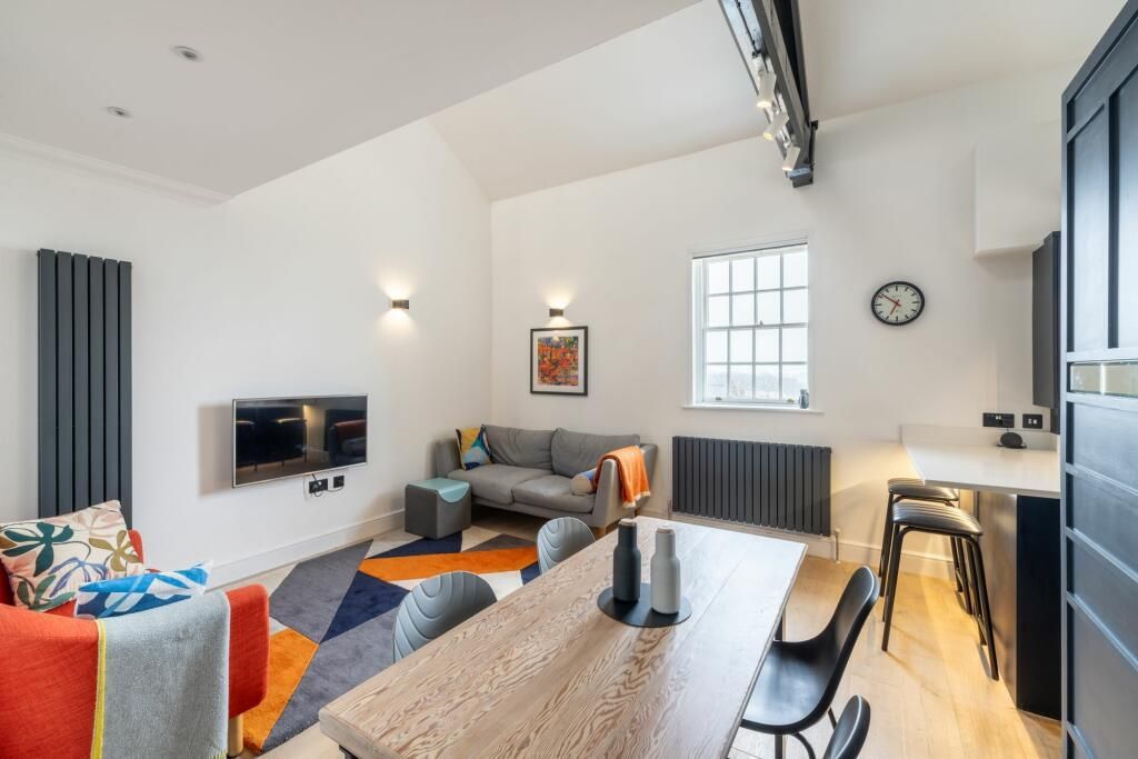 Bright modern living-dining room with gray sofa, orange chair, wall TV, and black dining table