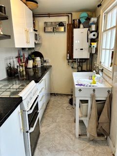 Narrow galley kitchen with white appliances, black countertops, and a utility sink by the window.
