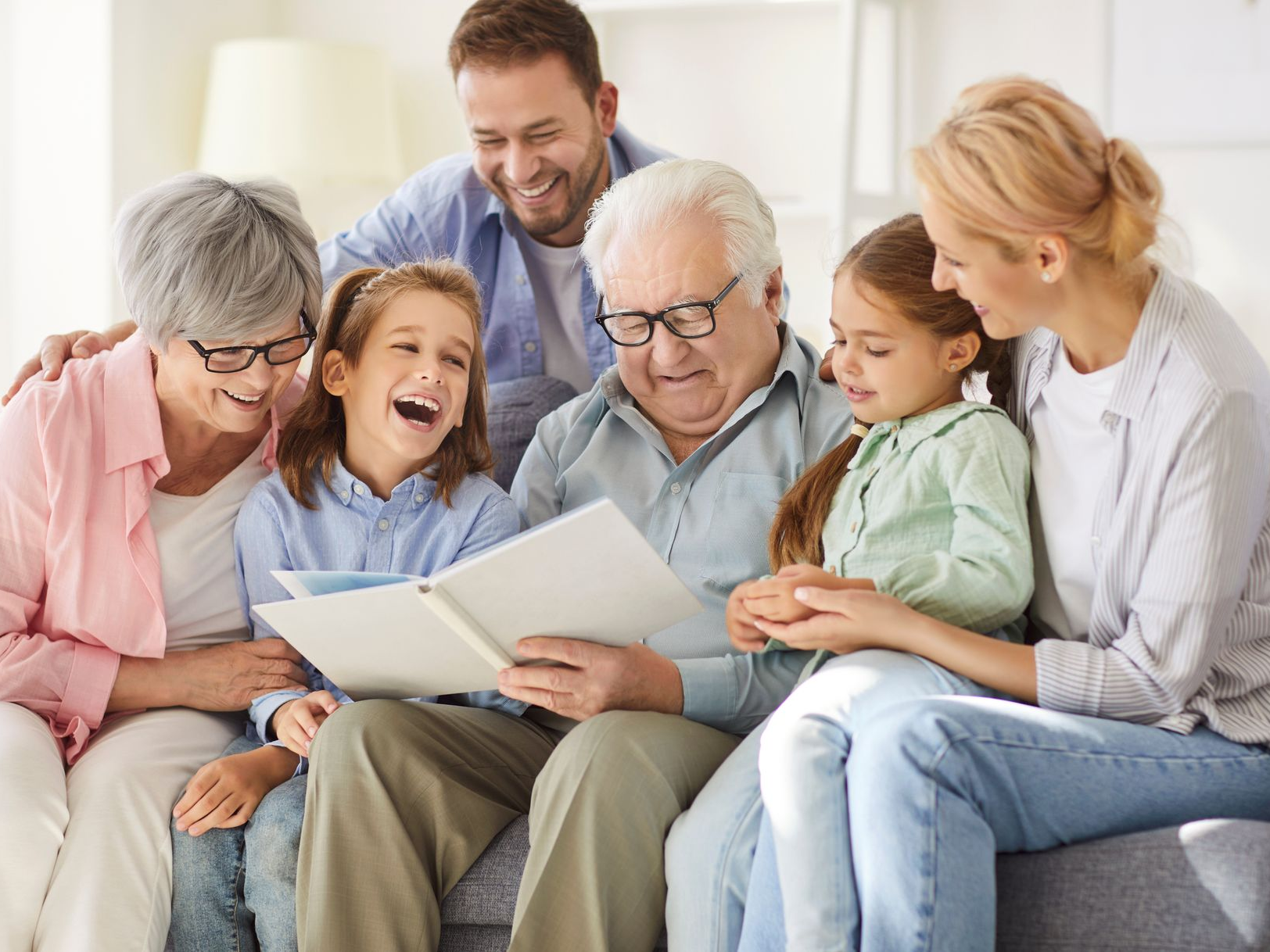 Famille regardant un album photo sur un canapé ; sourires et rires partagés dans un décor de salon.