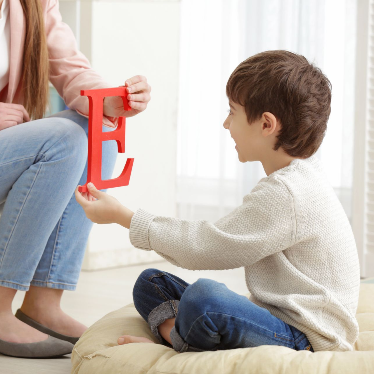 Femme et enfant tenant une lettre rouge « E », probablement dans un environnement d'apprentissage.