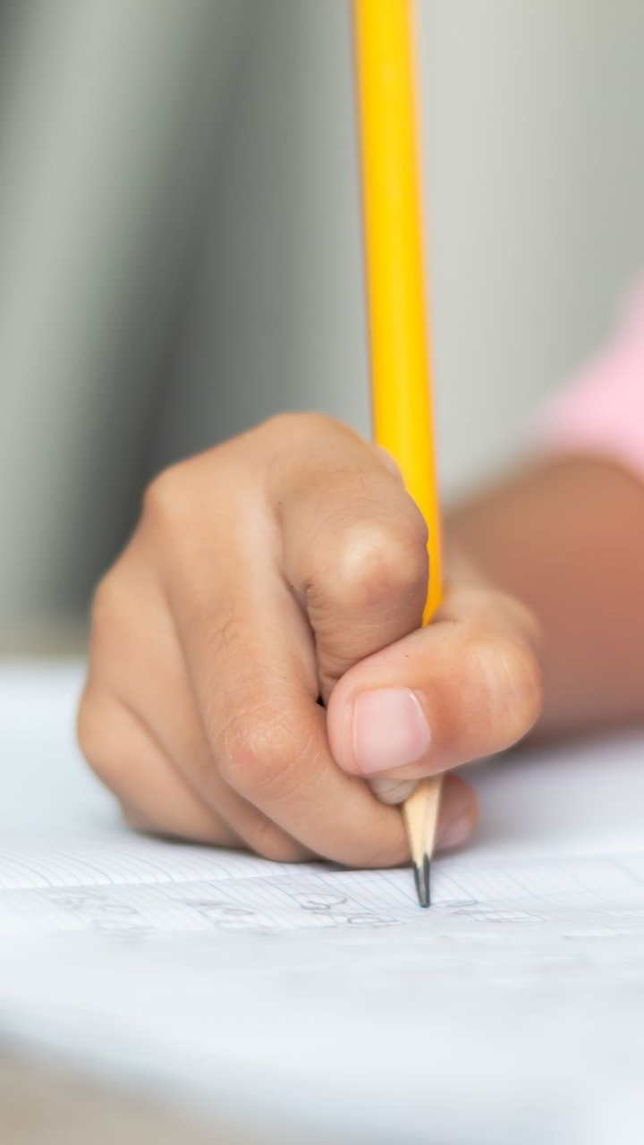 Main d'enfant tenant un crayon jaune et écrivant sur une feuille blanche. Gros plan, éclairage tamisé.