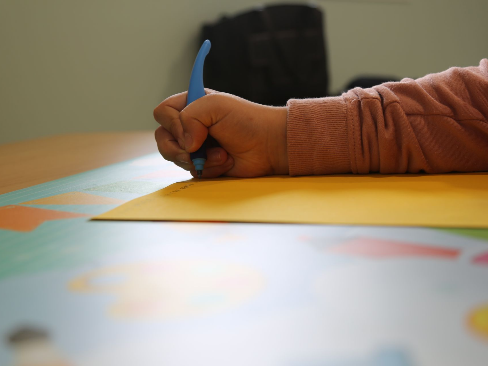 Jeune fille écrivant avec un crayon dans un cahier, expression concentrée, chemise rose, table en bois.