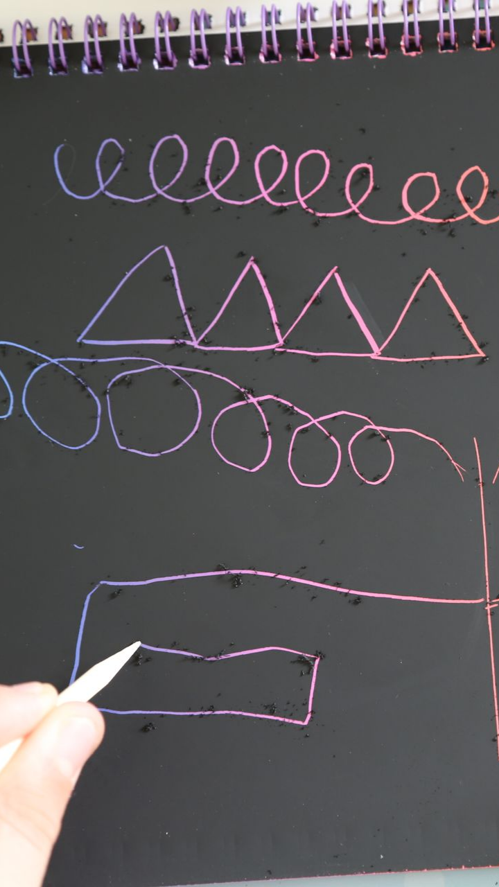 Mains d'enfant écrivant dans un cahier avec un crayon, pratiquant des formes cursives sur une surface en bois.