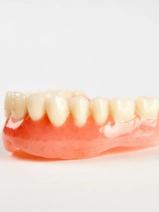 Primer plano de una dentadura postiza superior sobre fondo blanco. Base rosa con dientes blancos y beige.