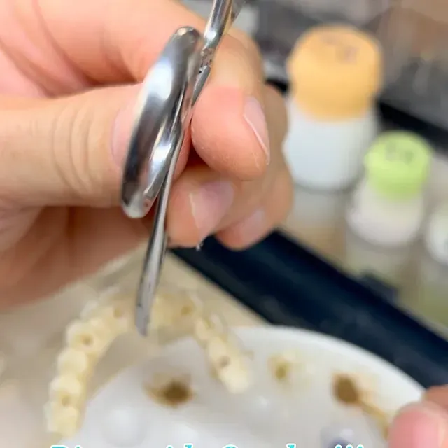 Mano sosteniendo una herramienta dental de plata sobre un molde dental con dientes blancos.