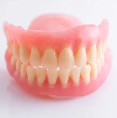 Dentadura postiza completa, línea de encías rosada y dientes blanquecinos, sobre una superficie blanca.