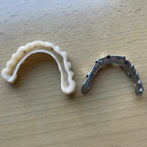 Dos guías para implantes dentales; una blanca, otra de metal, sobre una superficie de madera.
