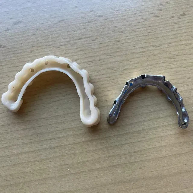 Dos guías para implantes dentales, una de plástico blanco y otra de metal plateado, descansan sobre madera.