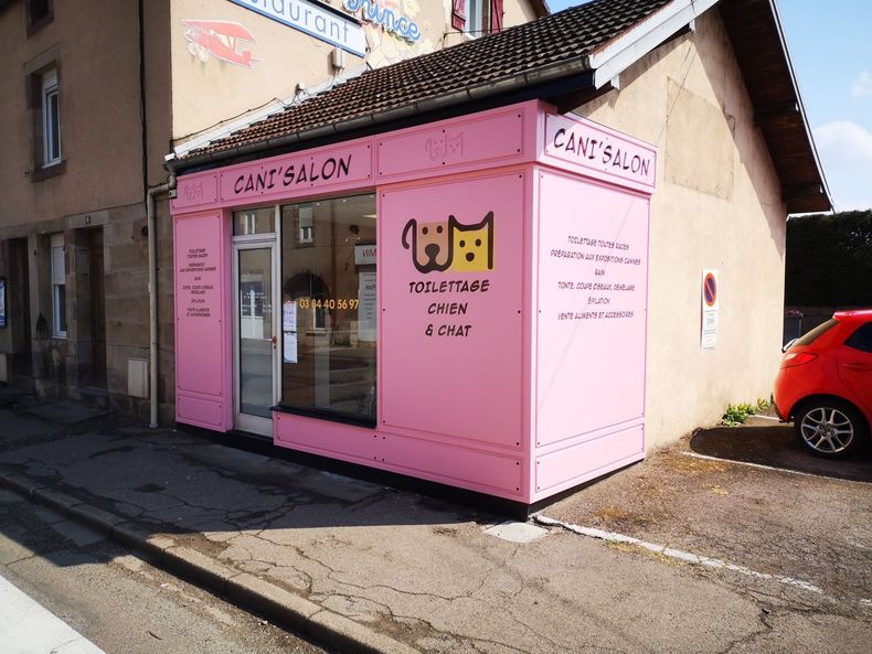 Devanture d'un salon de toilettage rose avec une enseigne peinte.
