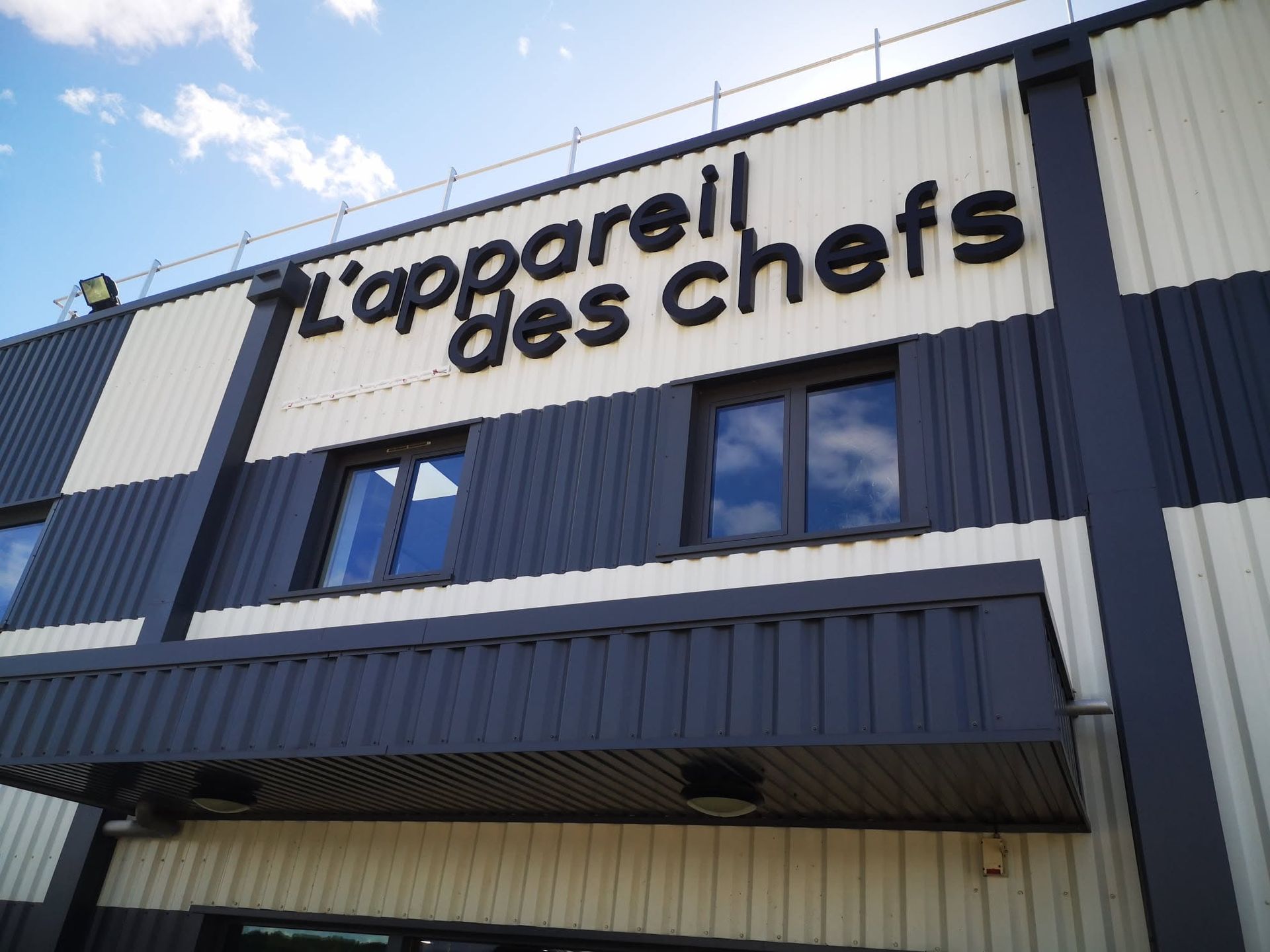 Enseigne de magasin sur un bâtiment bleu foncé et blanc sous un ciel bleu.