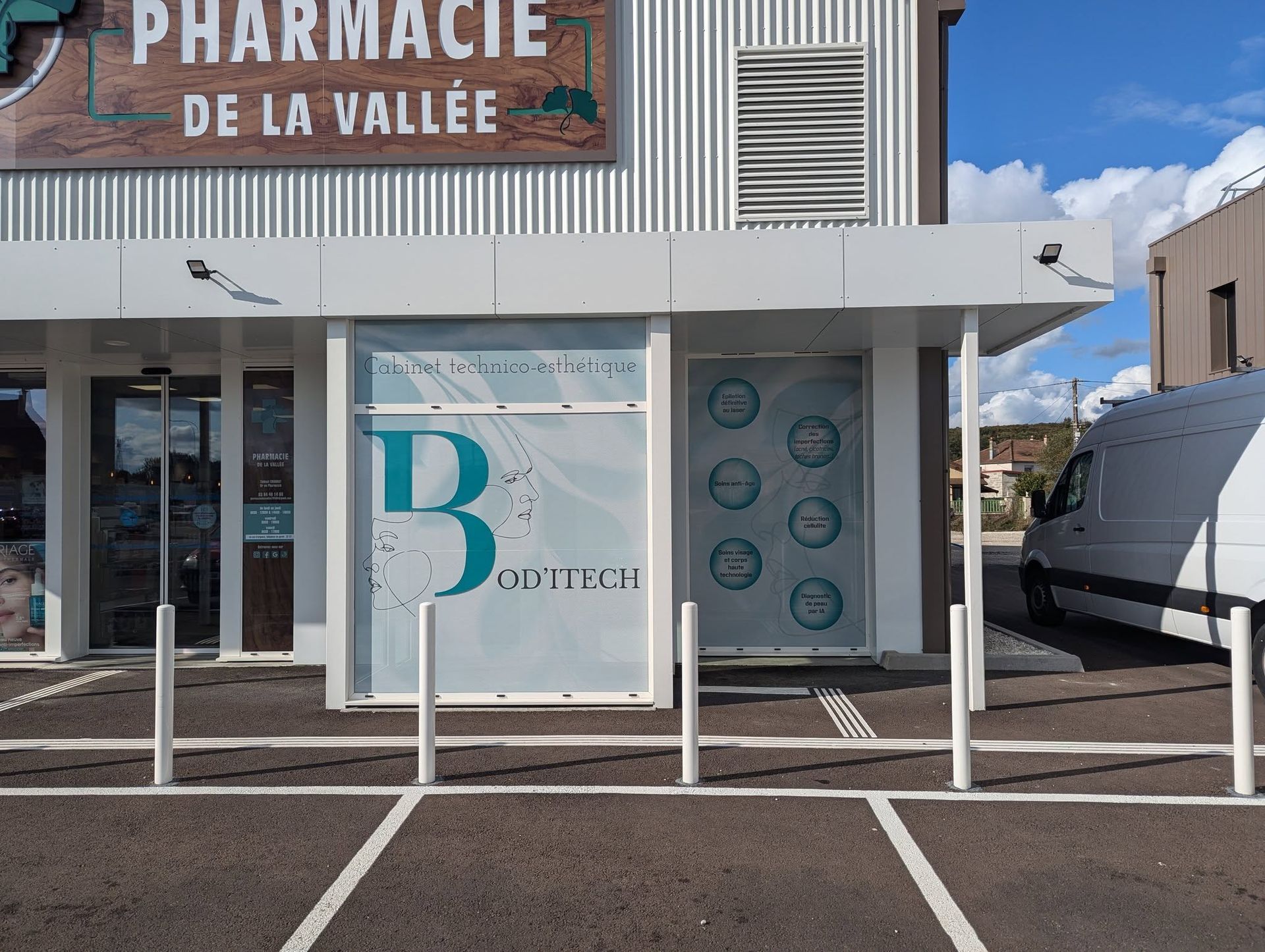 Extérieur de la Pharmacie de la Vallée avec une façade blanche, des portes vitrées et une camionnette garée à proximité.