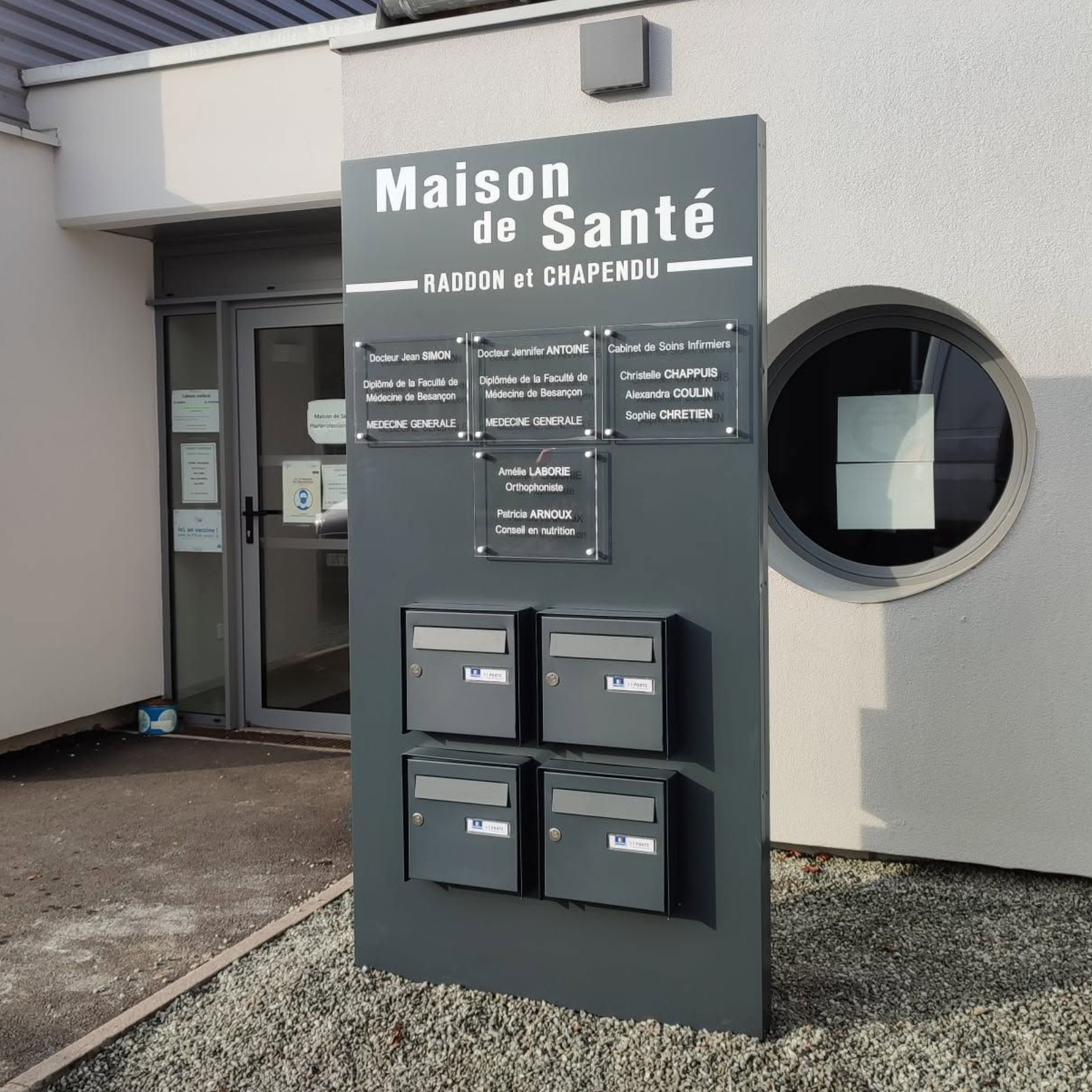 Panneau d'entrée du centre médical Maison de Santé, avec des boîtes aux lettres à l'extérieur d'un bâtiment gris.