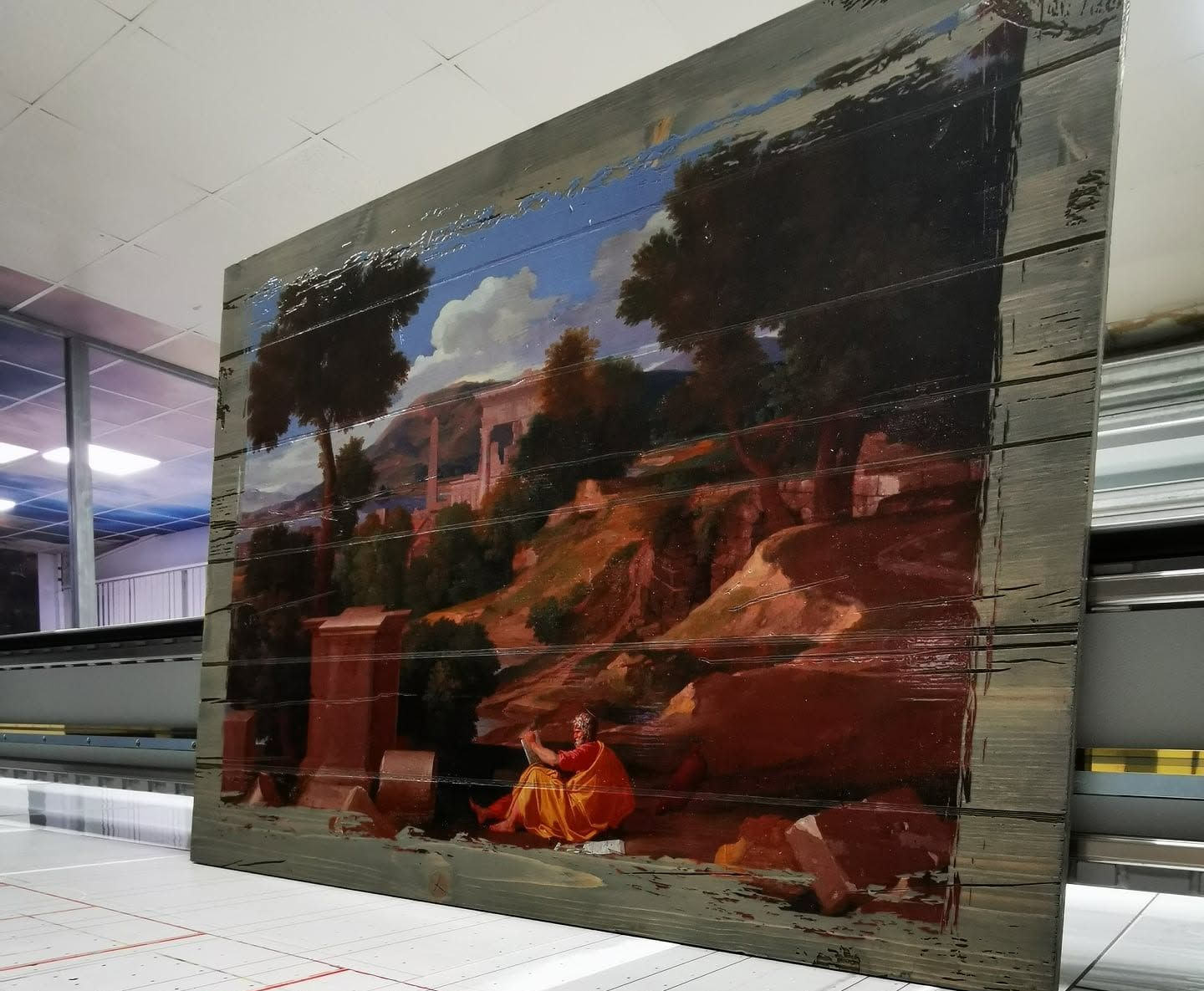 Fresque représentant une femme assise en robe colorée devant un paysage rocheux et un bâtiment sous un ciel bleu.