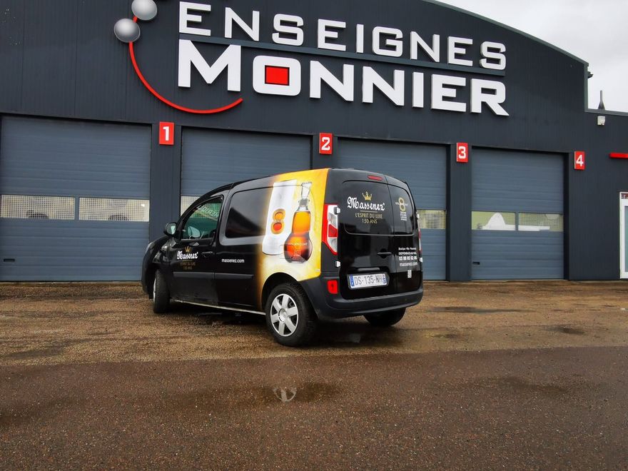 Une camionnette noire floquée est garée devant le magasin Enseignes Monnier.