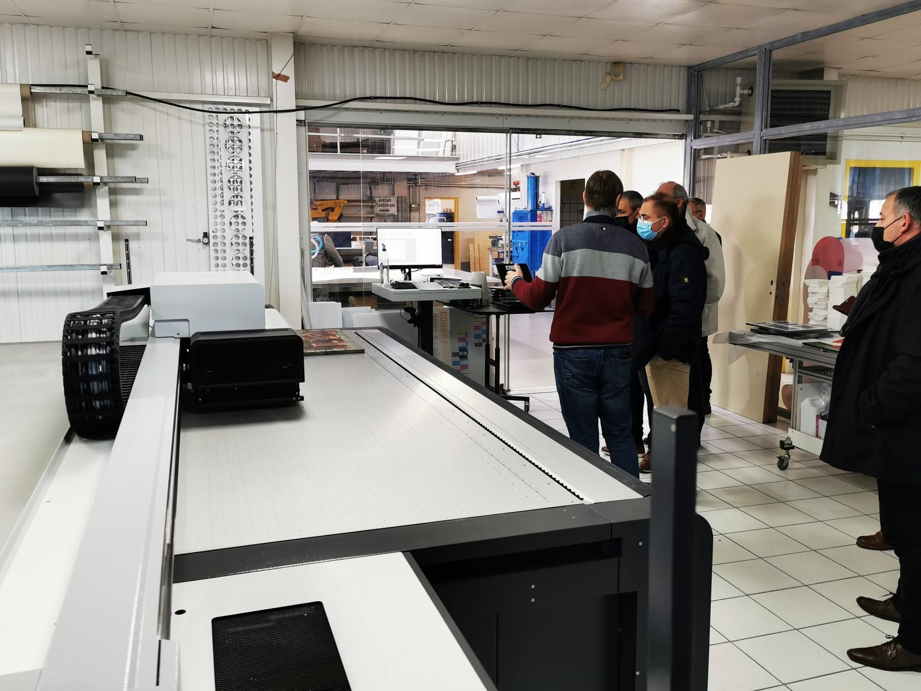Des personnes se tiennent debout dans une cuisine industrielle lumineuse, à côté de longues tables de préparation et de comptoirs métalliques.