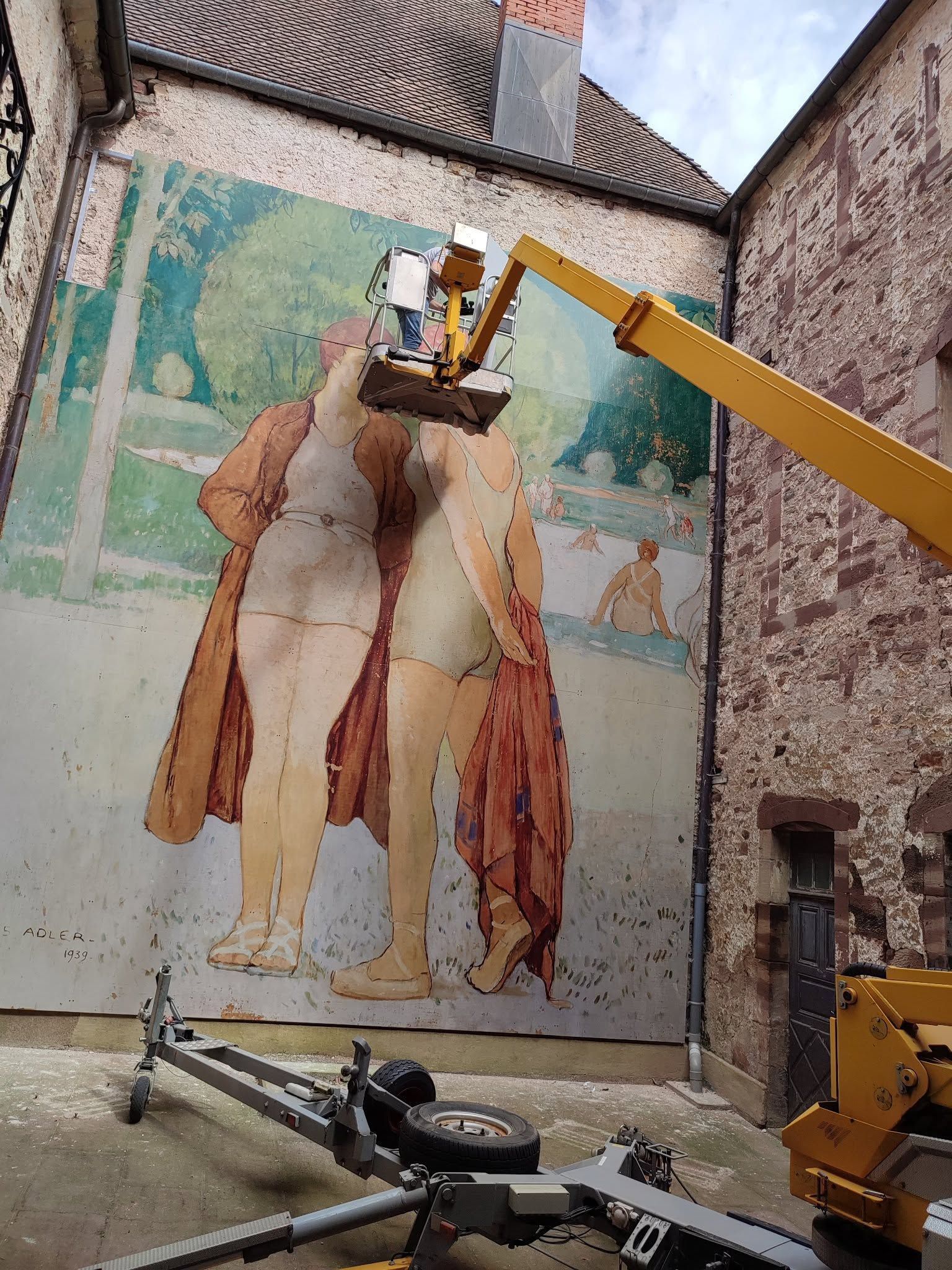 Une grue élévatrice retire un panneau mural d'un mur de briques d'une cour intérieure.