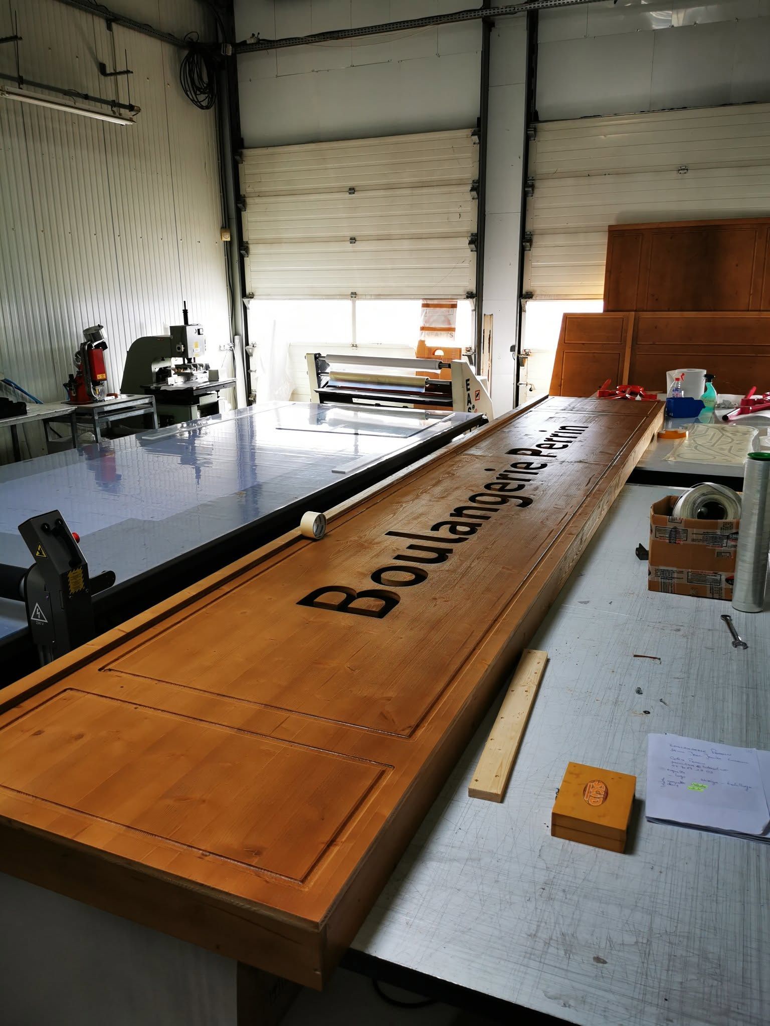 Grande planche en bois dans un atelier, entourée d'outils et de tables.