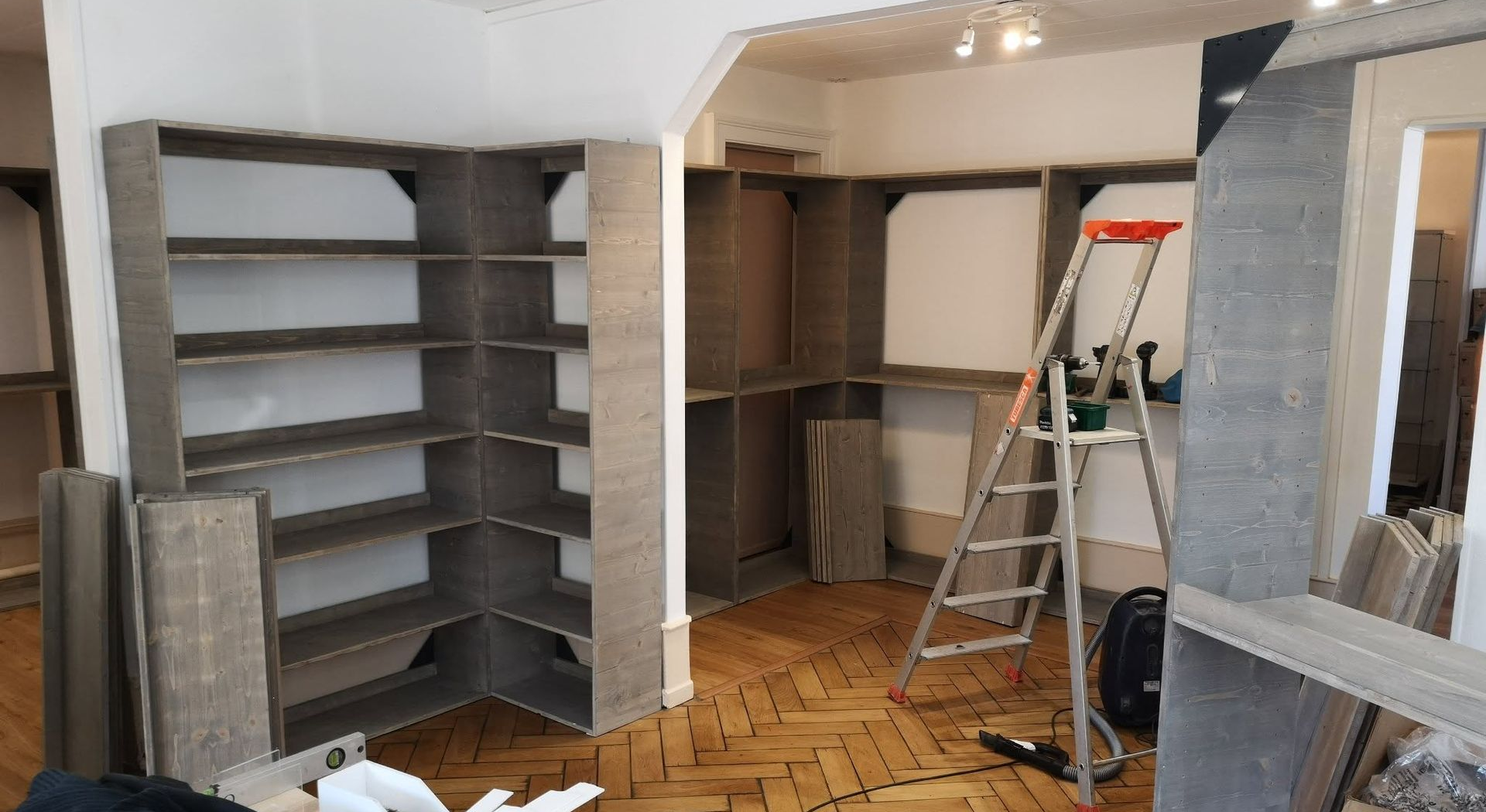 Pièce inachevée avec étagères intégrées, échelle et outils de peinture en cours de rénovation.