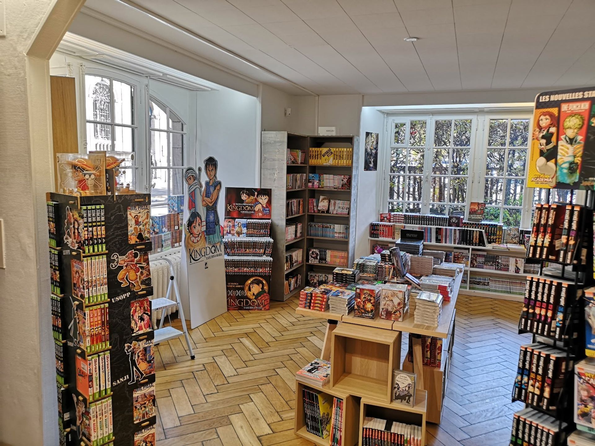 Allée de librairie avec des présentoirs à magazines colorés, des tables d'exposition et des étagères près d'une grande fenêtre.