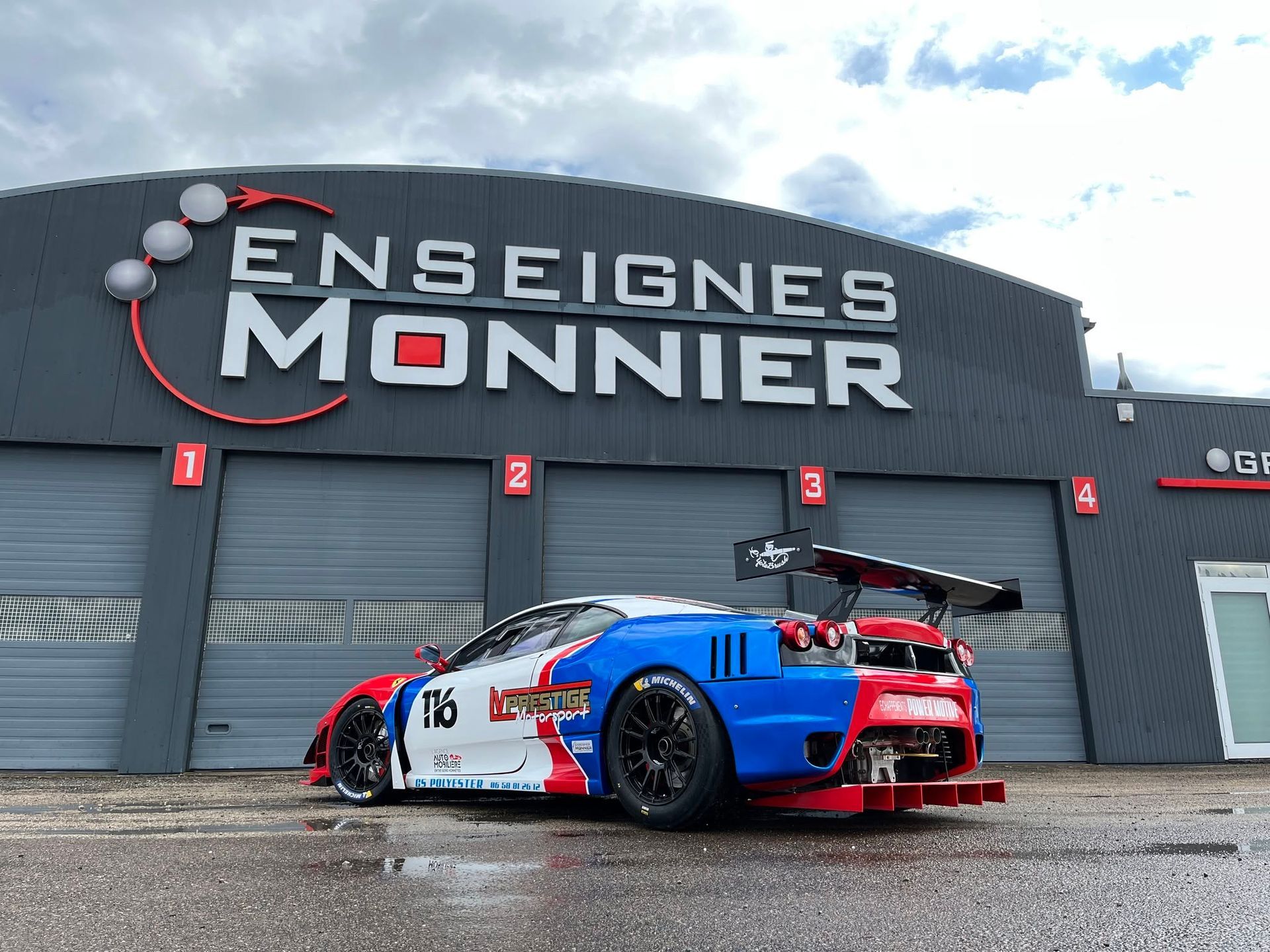 Voiture de course bleue et rouge garée devant l'entreprise Enseignes Monnier.