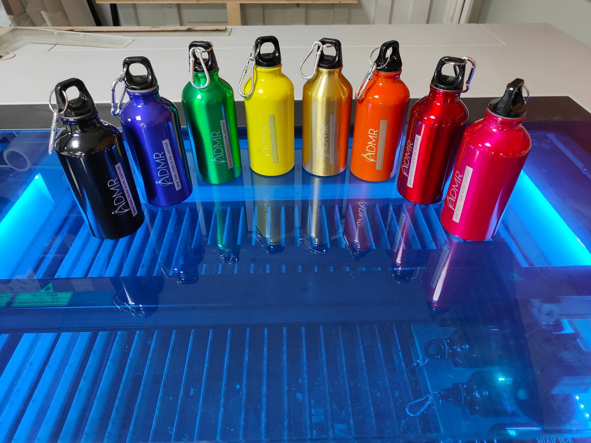 Rangée de bouteilles d'eau métalliques colorées sur une surface éclairée en bleu.