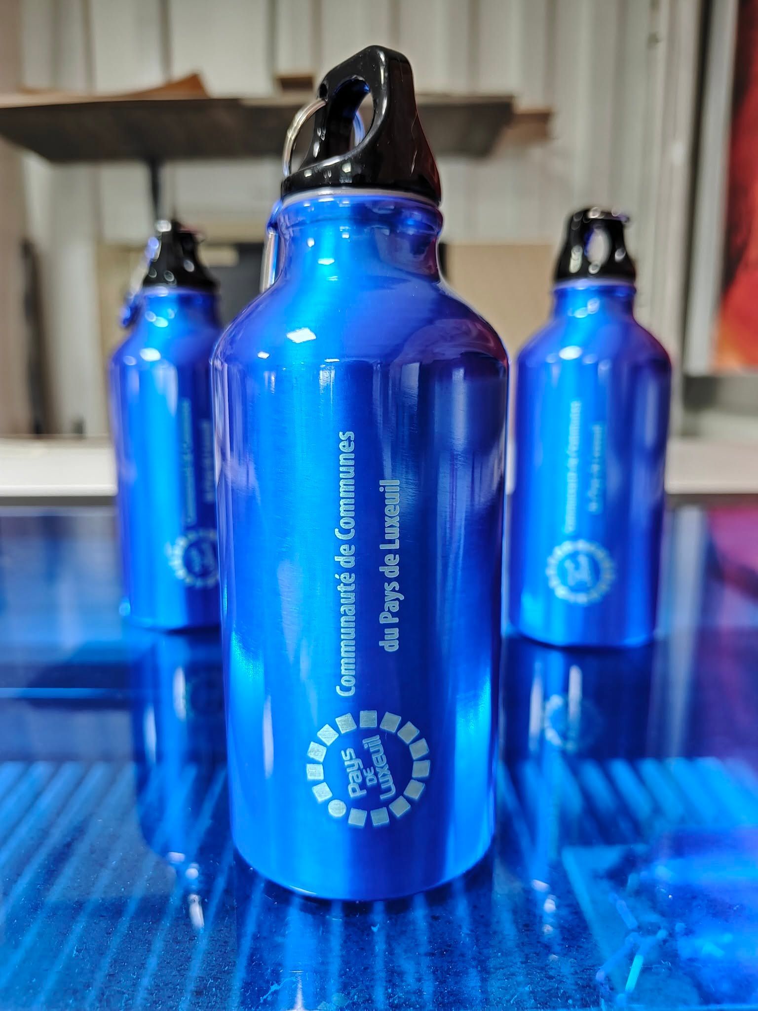 Bouteilles réutilisables bleues avec bouchons noirs sur fond bleu, une bouteille étant placée au centre, au premier plan.
