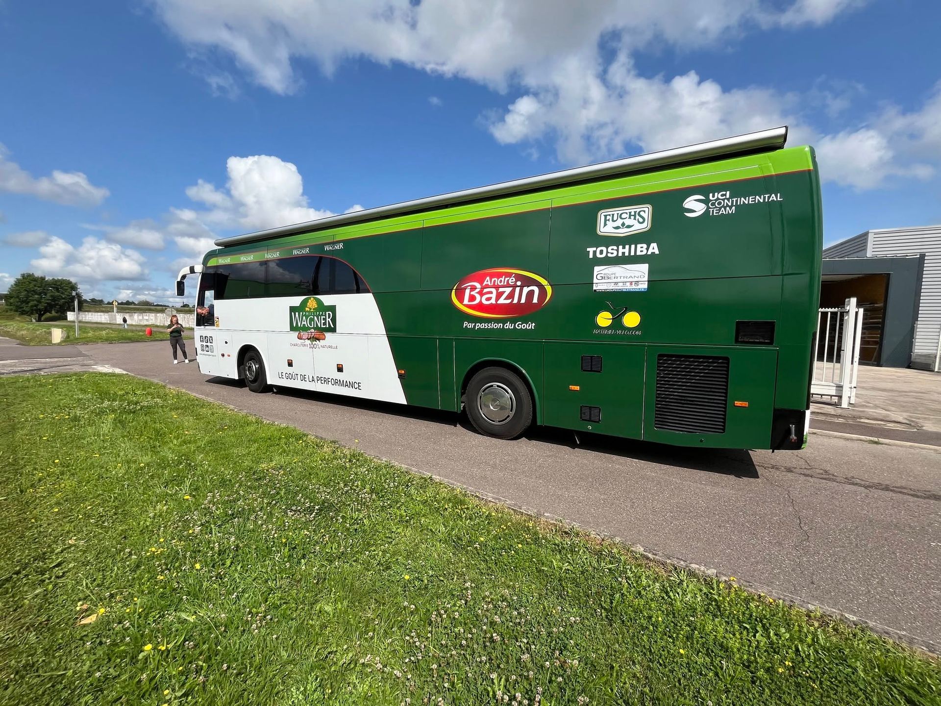 Un autocar vert et blanc est garé en bord de route sous un ciel bleu nuageux.