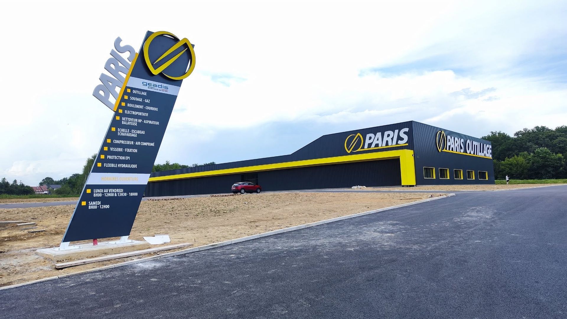 Bâtiment avec une façade bleue et jaune, situé à côté d'une route goudronnée et d'un panneau sur un terrain en gravier.