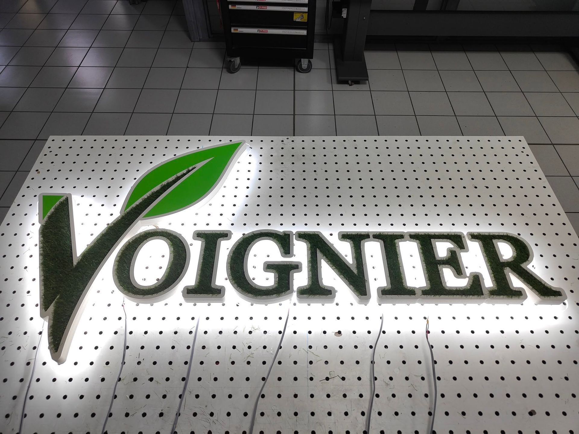 Logo Voignier sur une surface blanche perforée avec un accent de feuille verte.