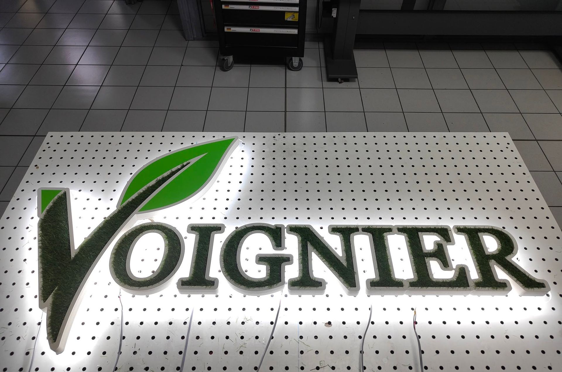 Logo Voignier sur un sol carrelé avec lettrage noir et accent de feuille verte.