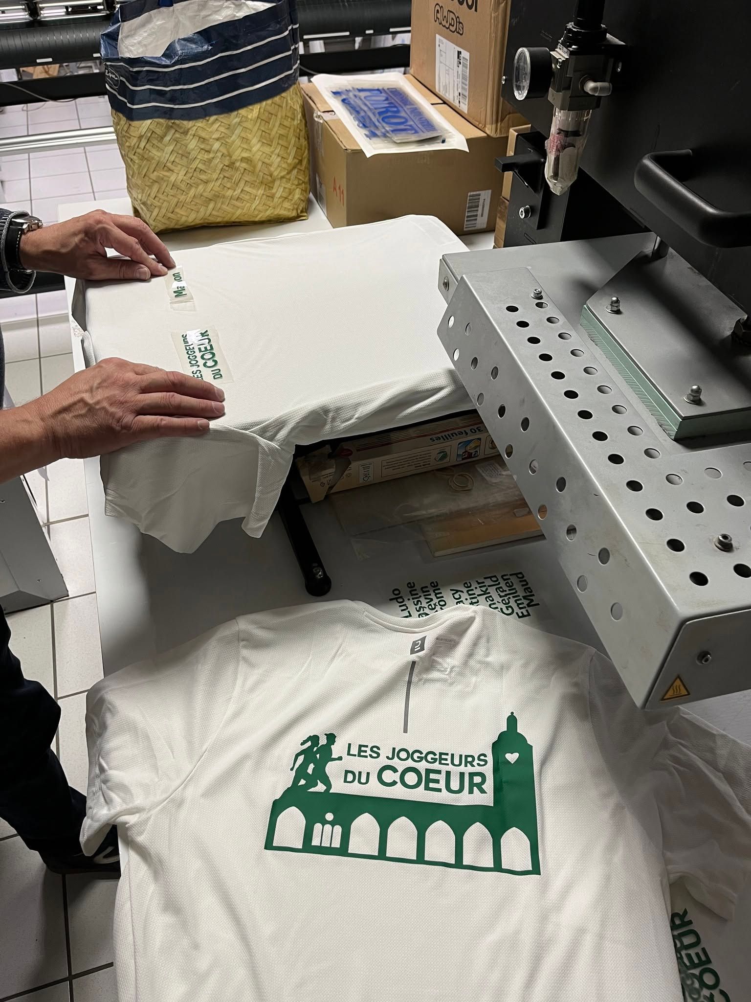 Des mains plient un t-shirt blanc sur une presse à sérigraphier.
