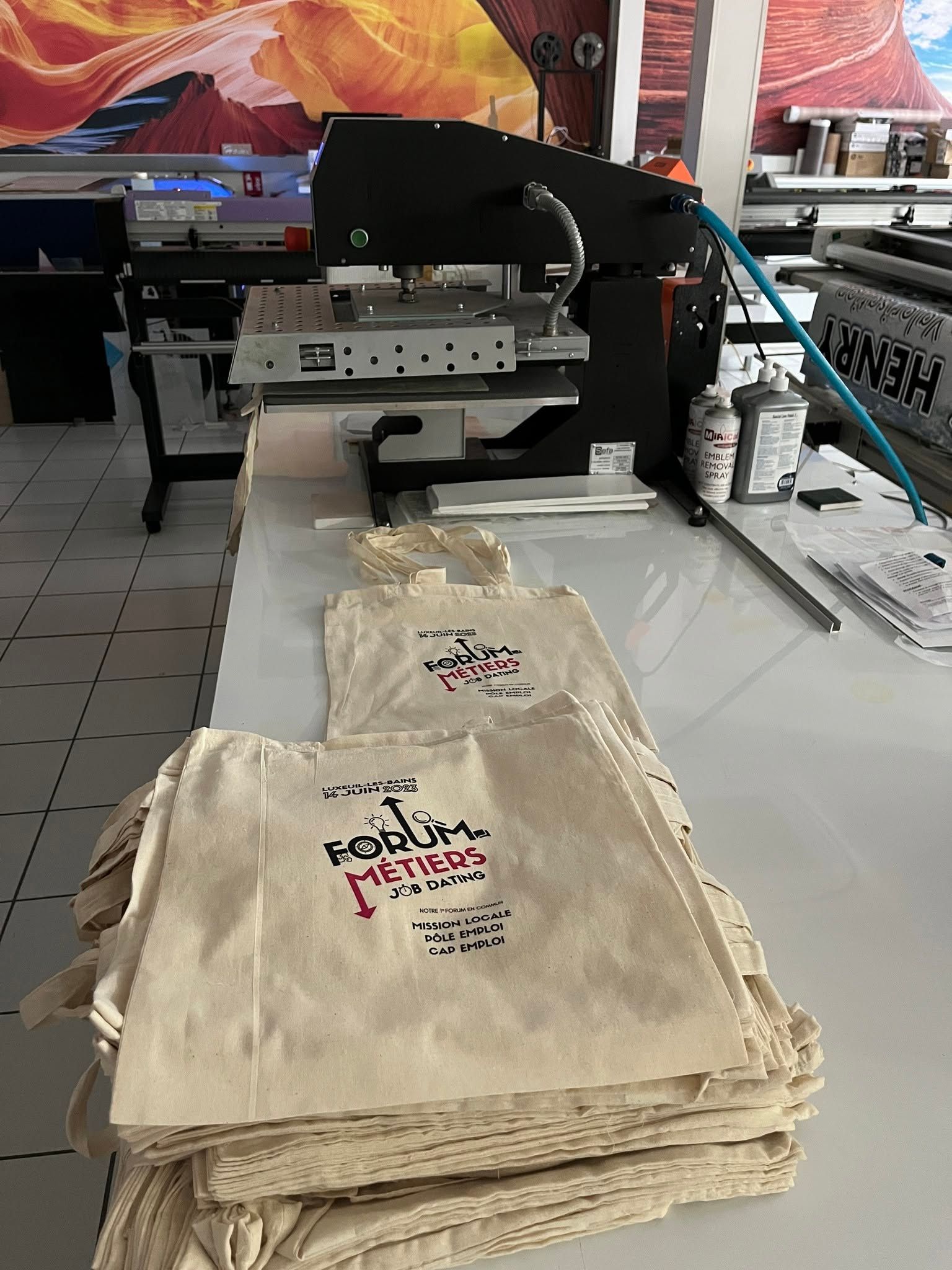 Des sacs cabas beiges empilés sur une table dans un atelier.