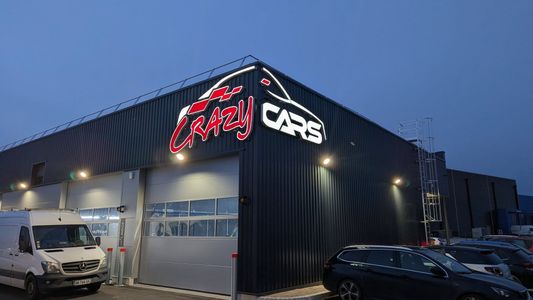 Façade Crazy Cafe au crépuscule, avec extérieur noir, enseigne lumineuse et véhicules stationnés