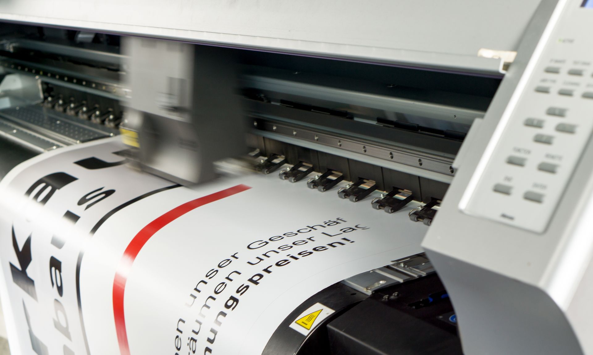 Imprimante grand format imprimant une feuille couleur avec des marquages noirs et rouges.