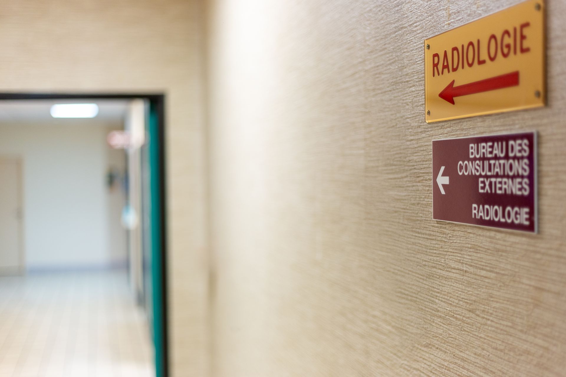 Couloir d'hôpital avec des panneaux indiquant les services de radiologie et de consultation sur un mur beige.