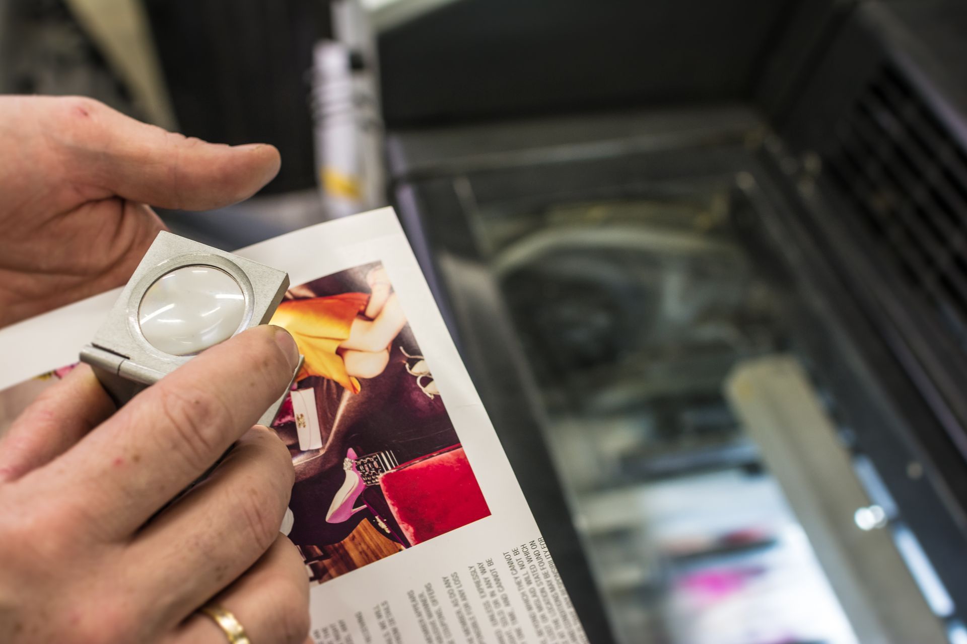 Main tenant une loupe au-dessus d'une page de magazine avec une photo et du texte en couleur.