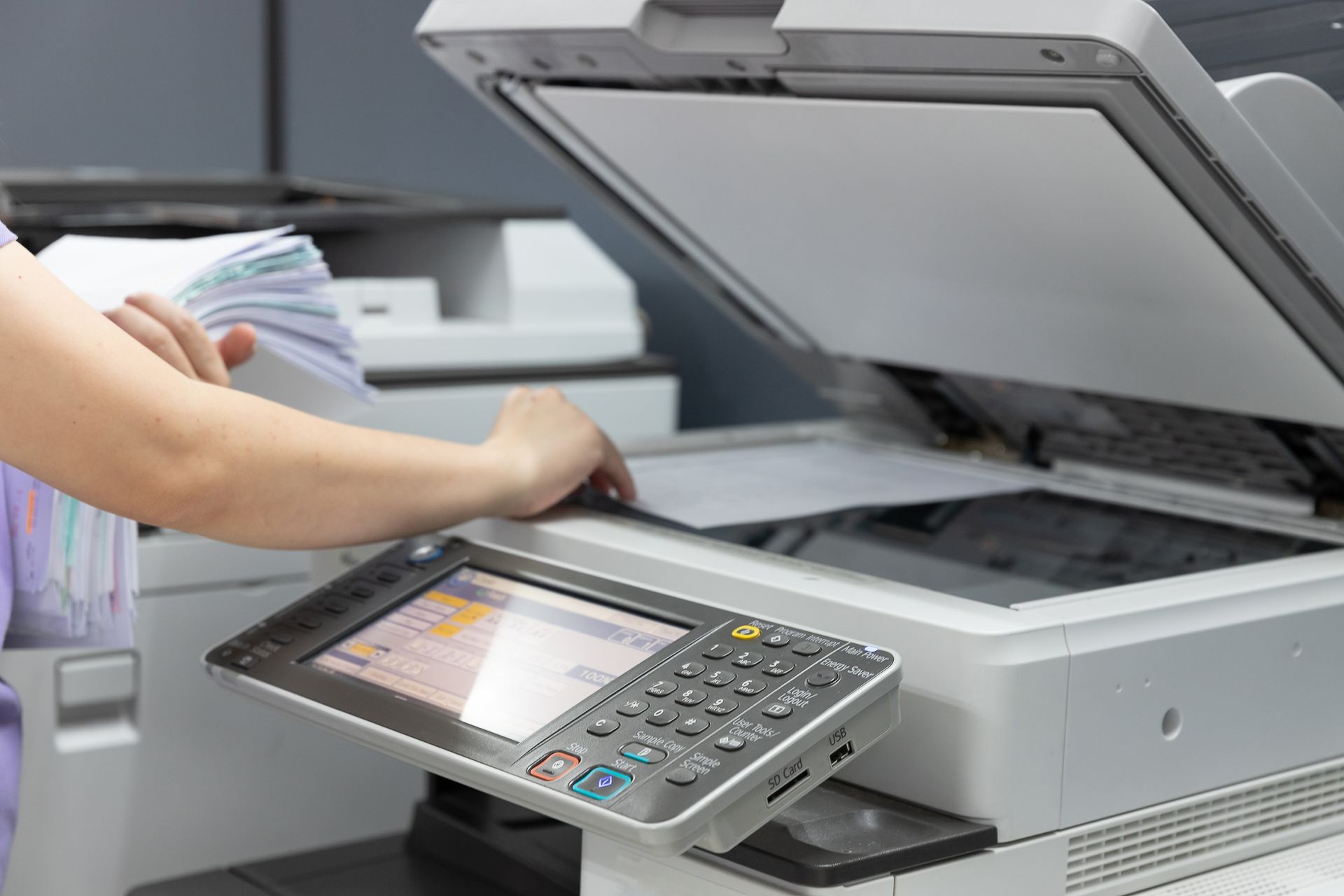 Une personne manipule un photocopieur avec le couvercle du scanner et le panneau de commande ouverts dans un bureau.
