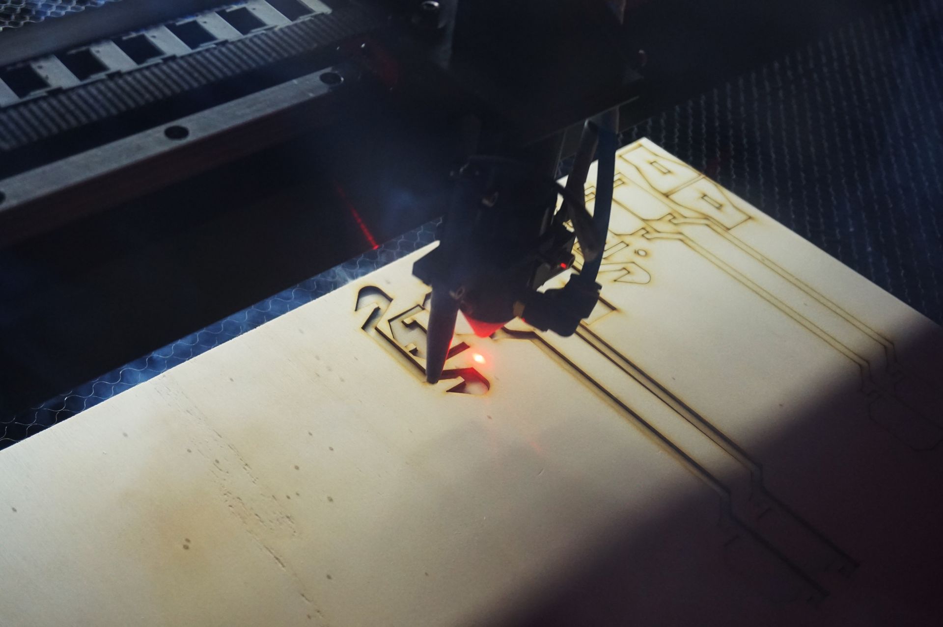 Découpeuse laser gravant une planche de bois dans un atelier sombre.