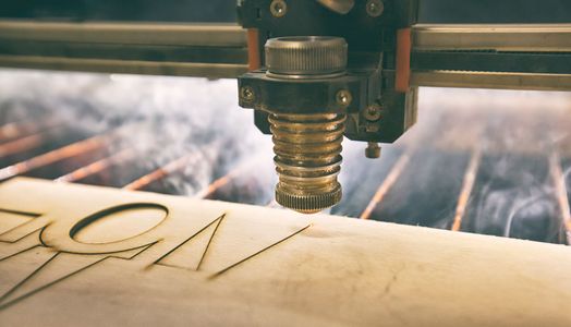 Gravure de lettres au laser sur une planche de bois dans un atelier.