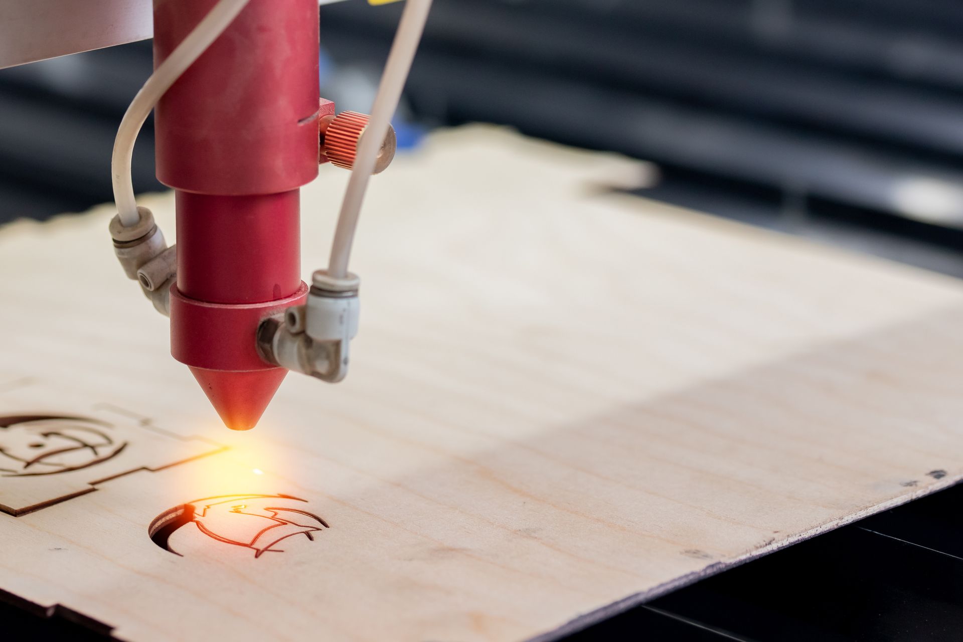 Découpeuse laser gravant une planche de bois avec un faisceau rougeoyant.