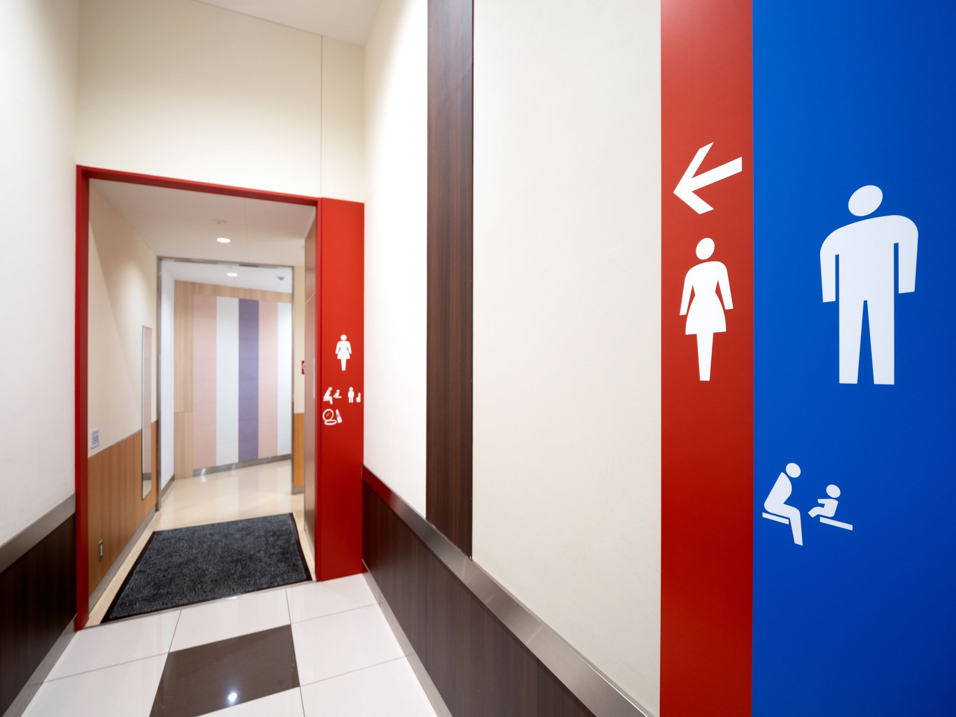 Couloir avec des panneaux de toilettes rouges et bleus et une porte ouverte donnant sur l'intérieur.